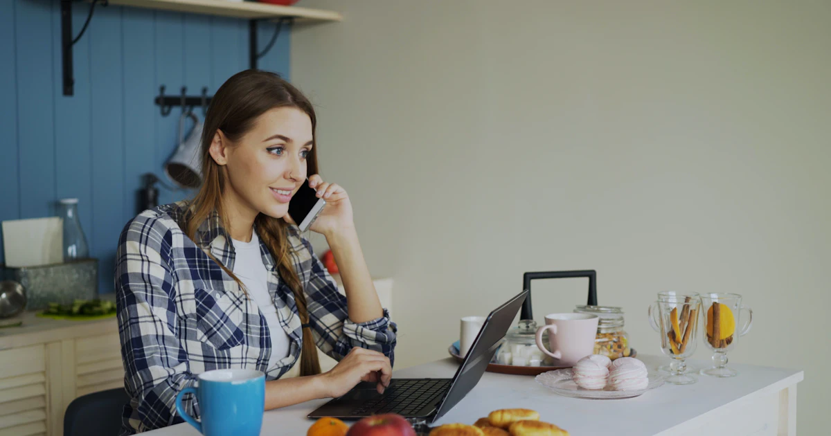 Frau, die telefoniert, während sie am Laptop am Tisch arbeitet
