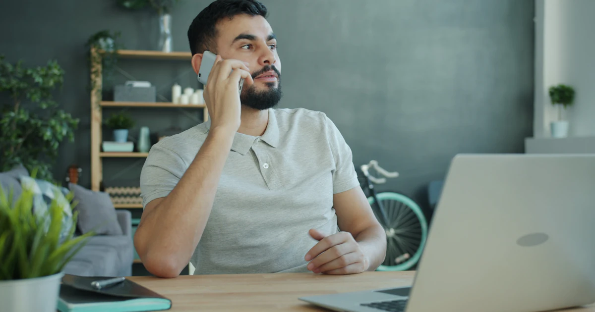 Mann telefoniert am Schreibtisch mit Laptop