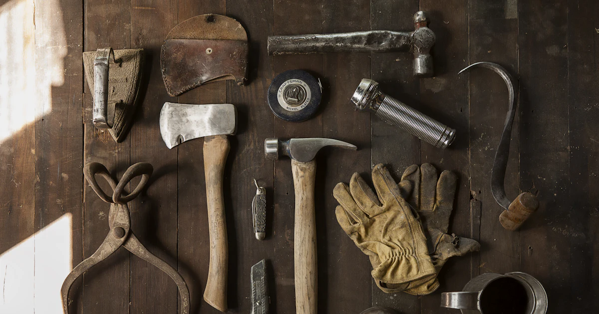 Vintage-Werkzeuge wie Axt, Hammer, Handschuhe und Metallwerkzeuge auf dunklen Holzbrettern