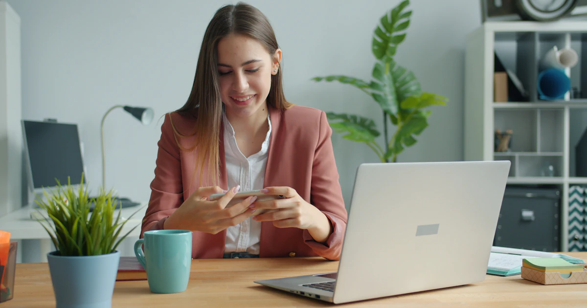 Junge Frau, die an einem Schreibtisch mit Laptop und Laptop arbeitet
